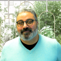 Man with salt-and-pepper beard, in casual sweater, in front of ornate window overlooking garden